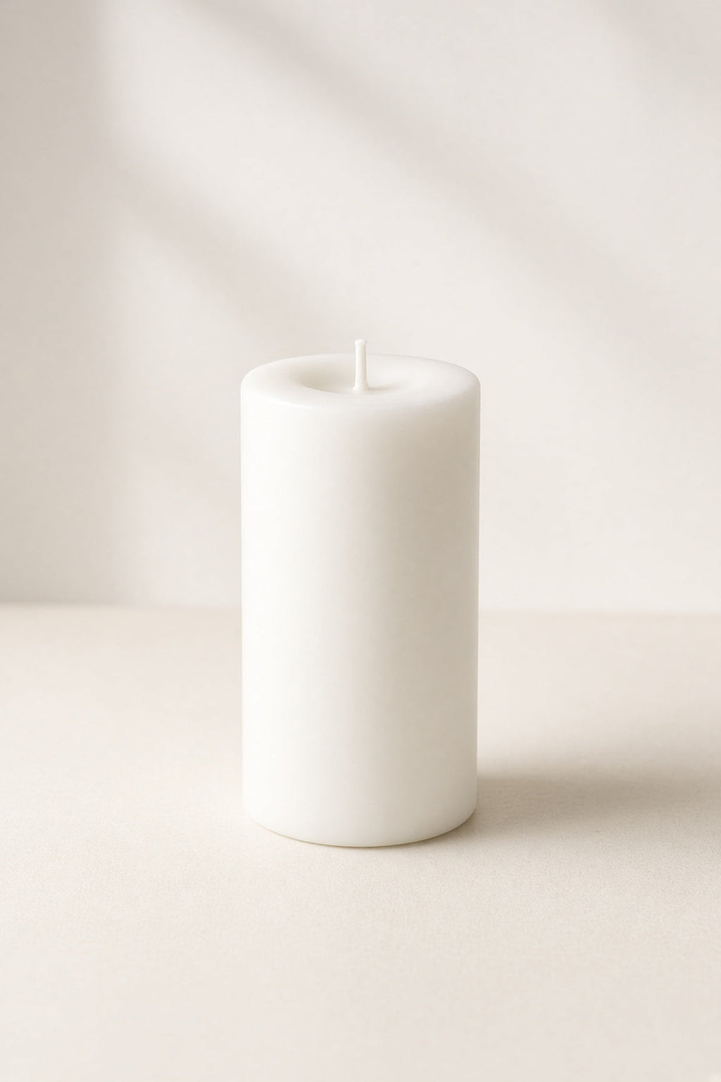 Smooth white unscented pillar candle on cream background
