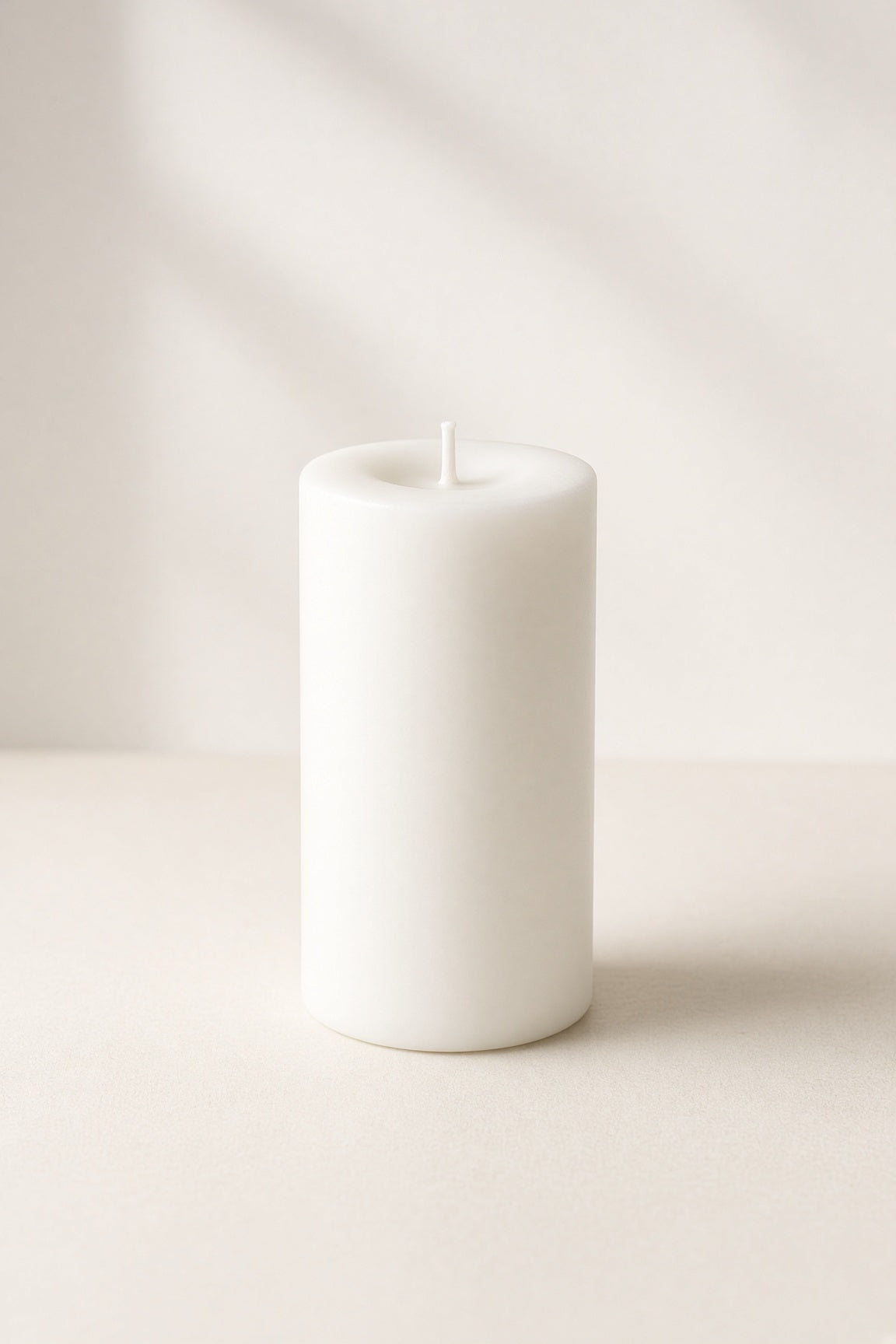 Smooth white unscented pillar candle on cream background